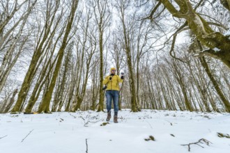 Man in a yellow jacket and beanie enjoying a winter adventure, holding a camera and phone while