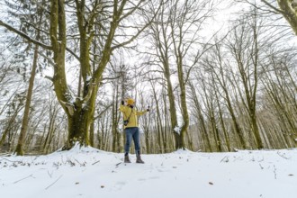Man in yellow jacket and beanie enjoying a solitary winter hike, standing in a snow covered forest