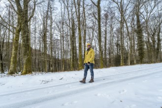Man in a yellow jacket, beanie, and sunglasses exploring a snow covered forest path, enjoying the