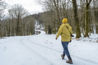 Man with camera backpack trekking a winding snowy path through a bare winter forest, enjoying