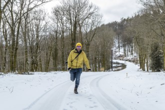 Cheerful man in a yellow jacket and hat joyfully running on a snow covered forest path, expressing