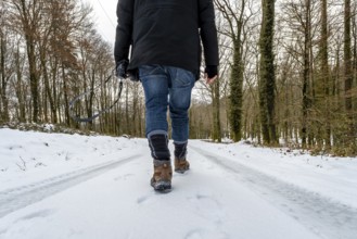 Person walking alone down a snow covered forest road in winter, wearing hiking boots and carrying a