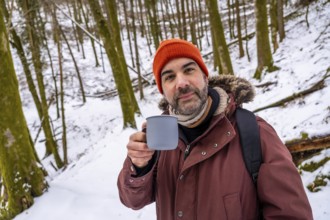 Man with an orange beanie and a winter coat holding a mug of a hot beverage, finding warmth and