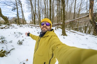 Man posing for a selfie during a winter hike, exploring a snowy forest landscape with bare trees