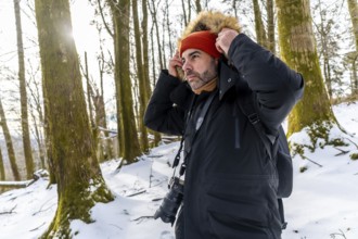 Man photographer adjusting his jacket or coat hood with fur trim while wearing a beanie and scarf