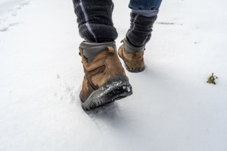 Person walking through fresh white snow in sturdy brown hiking boots and warm socks, leaving
