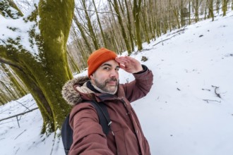 Man posing for a selfie in a snowy forest during winter, looking out with his hand shading his