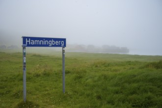 Town sign for Hamningberg on the Barents Sea in the midst of grassy landscape with fog and calm