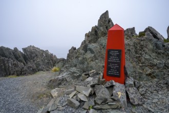 Red memorial to resistance fighters from the Second World War on rough rocks with fog in Norway,