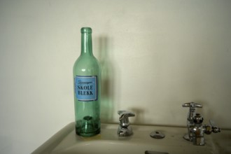 Green bottle with the Norwegian inscription Schukl ink a sink in front of a simple wall with retro