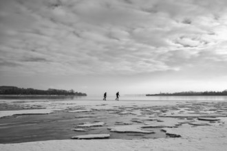 Two people walk across an icy water surface under a cloudy sky, black and white photography,