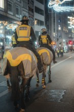 Police officers on horses patrol a brightly lit city street at night, London, England, Great