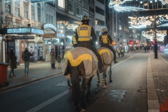 Police horses patrol an illuminated city street at night, surrounded by pedestrians and bright