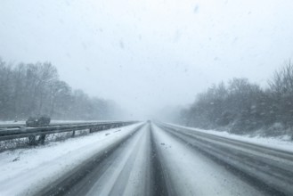 View through the windshield of a passenger car driving through light snowblowing on partly