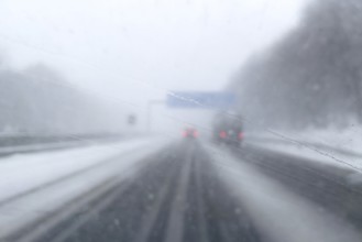 View through fogged windshield of cars driving through light snowblowing on partially covered