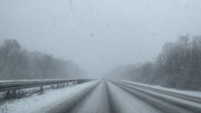 View through the windshield of a passenger car driving through light snow on an empty, partially
