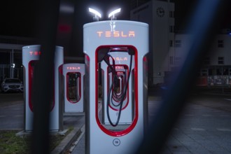 Several Tesla charging stations at night in bright red under city lights, Tesla Supercharger,