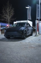 A black Tesla at night in a parking lot at a charging station, New Model Y Standard, Tesla