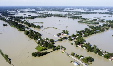 An aerial view shows widespread flooding submerging villages and farmland, with isolated homes and