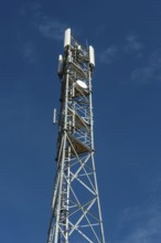 Tall silver telecommunications tower extends to a blue sky with wispy clouds on a sunny dayA tall