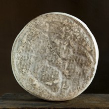 Saint-Nectaire cheese is displayed against a dark backdrop, highlighting the textured rind and