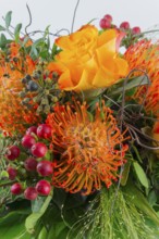 Colorful bouquet with orange and yellow flowers surrounded by red berries and green foliage,