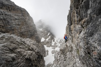 Mountaineer climbs the Via Ferrata Oliva Detassis via ferrata, steep cliffs covered in clouds,