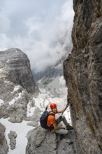Mountaineer climbs the Via Ferrata Oliva Detassis via ferrata, view of mountain basin with steep