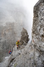 Mountaineers climb the Via Ferrata Oliva Detassis via ferrata in fog, steep mountains covered in