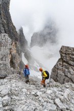 Two mountaineers in rocky, cloudy mountain landscape at Bochetta Bassa del Massodi, Brenta