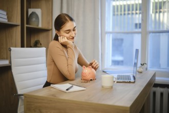 A woman is sitting at her desk in an office. She looks thoughtful while holding her chin in one