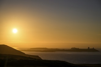 Midnight sun on Mount Domen in the background the city of Vardø, sea at sunset with golden sky and