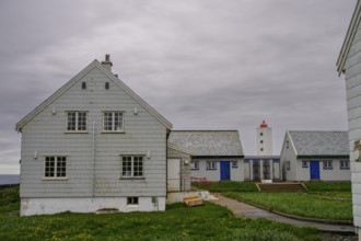 Lighthouse between blue and white houses rises under a grey sky Kjølnes Fyr, small windows and