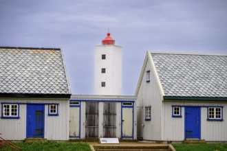 Lighthouse between two blue and white houses rises under a grey sky Kjølnes Fyr, small windows and