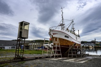 A large boat fishing trawler fishing vessel on a dry dock is positioned against a cloudy sky in the