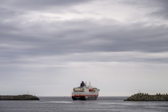 The Hurtigrouten Hurtigruten ship Kong Harald sails from Berlevag harbour, on the horizon with a