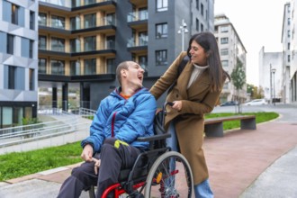 Man with a disability in a wheelchair laughing happily while a female caregiver pushes him along a