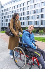 Caregiver pushing a man with a disability in a wheelchair outdoors, both smiling and sharing a