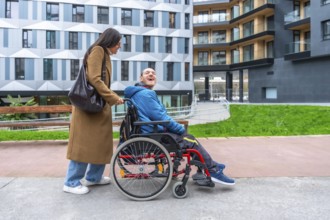Caregiver pushing a happy adult man with a disability in a wheelchair, enjoying time outdoors