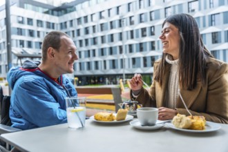 Young man in wheelchair having a joyful conversation and enjoying coffee with a female friend at an