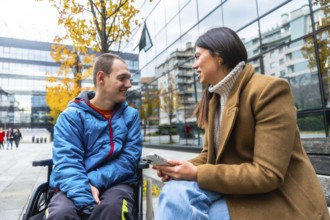 Man in wheelchair smiling and attentively listening to a woman sitting beside him on a bench,