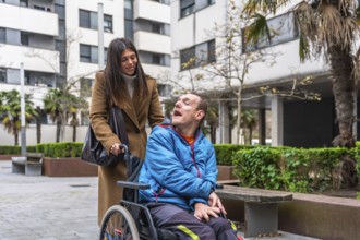 Woman pushing an adult man in a wheelchair, providing support and care during an urban outing,
