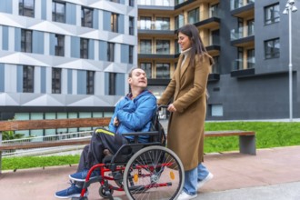 Young woman smiling as she pushes a man in a wheelchair along an accessible city street, showcasing