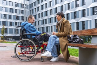 Man in a wheelchair and woman sitting on a bench engaging in a friendly conversation outdoors,