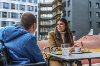 Woman and boy in a wheelchair share a warm, engaged conversation at an outdoor urban cafe, smiling