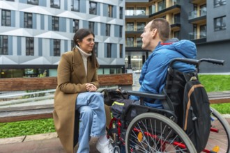 Woman and man with cerebral palsy sitting together by a bench, having a conversation in an urban