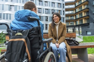Woman on urban bench smiling and listening attentively to man in wheelchair, sharing supportive