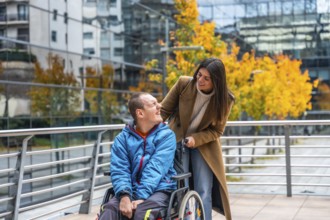 Support worker assisting a smiling disabled man in a wheelchair on an autumn day, navigating an