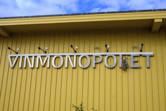 Yellow building of the Norwegian state wine monopoly with sign and floodlights and a breeding