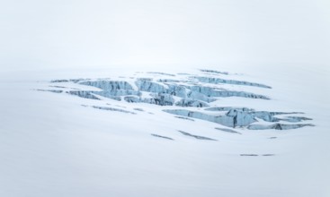 Smooth white snowy area on the glacier broken by crevasses with blue rugged glacial ice, detail,